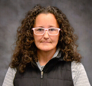 woman with curly hair wearing a black zip-up vest and glasses posing for the camera