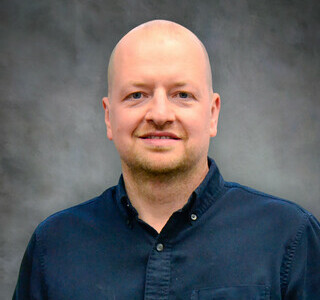 man wearing a dark blue button up shirt smiling for the camera