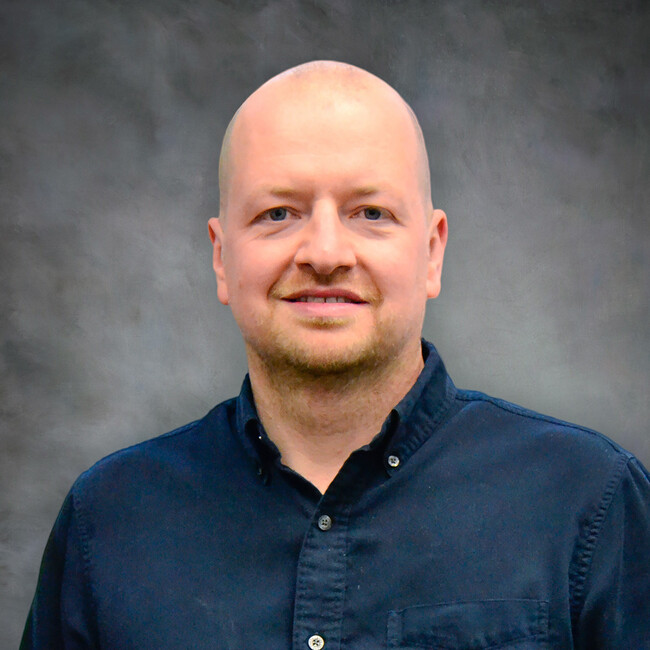 man wearing a dark blue button up shirt smiling for the camera