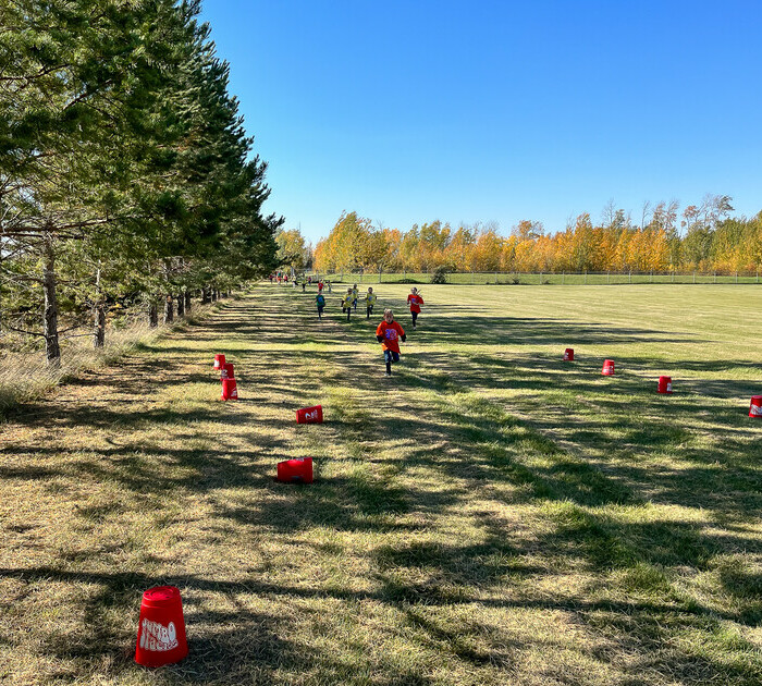 young students running through a field along the treeline