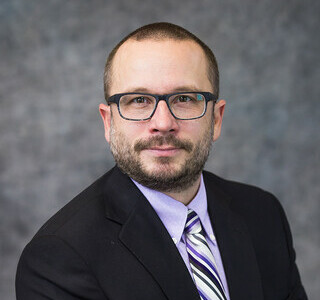 man wearing dark suit and glasses smiling for the camera