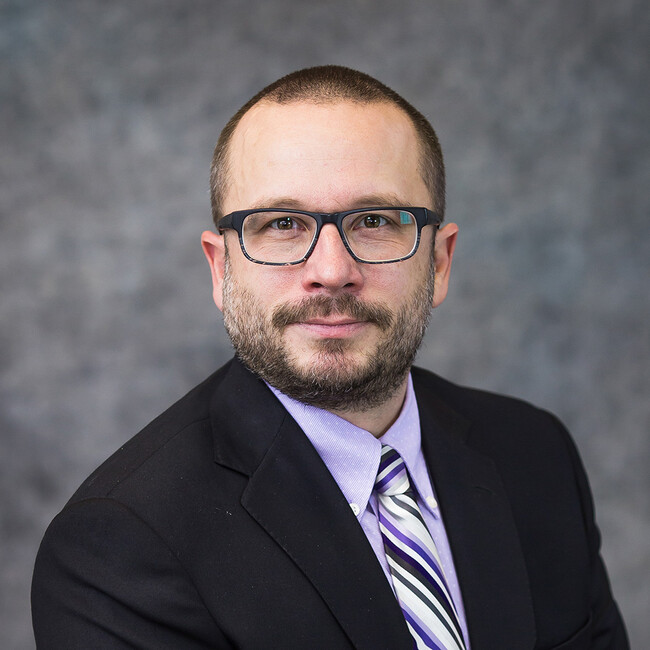 man wearing dark suit and glasses smiling for the camera