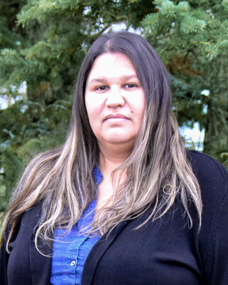 woman with long brown hair in front of an evergreen tree