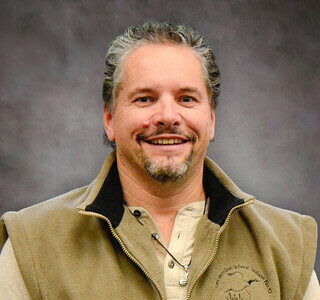 man wearing a beige zip-up vest smiling for the camera