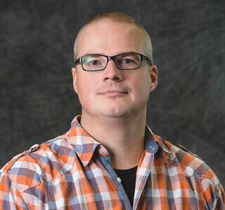 man wearing plaid shirt and glasses posing for the camera