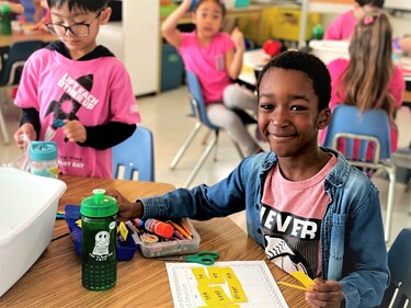 boy sitting in a classroom and smiling for the camera