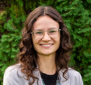 woman with dark curly hair and wire frame glasses smiling for the camera