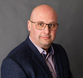 man in dark suit with glasses smiling for the camera