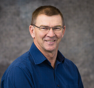 man with glasses wearing a dark blue button up shirt smiling for the camera