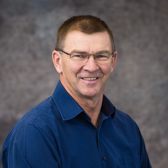 man with glasses wearing a dark blue button up shirt smiling for the camera