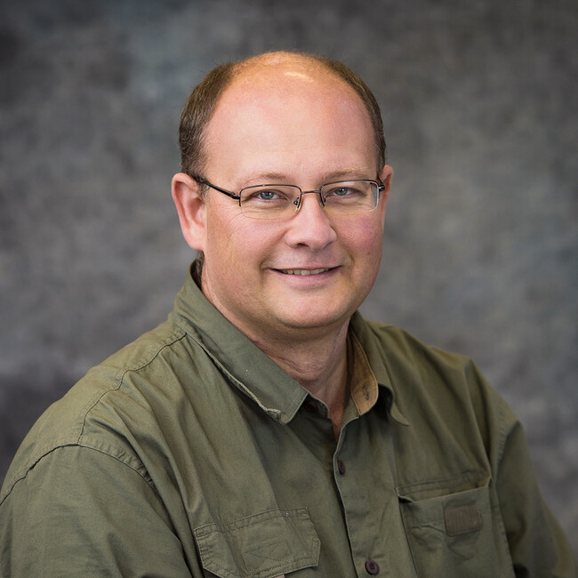 man wearing dark green button up shirt and glasses smiling for the camera