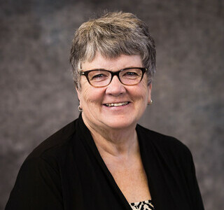 woman with short grey hair and glasses smiling for the camera