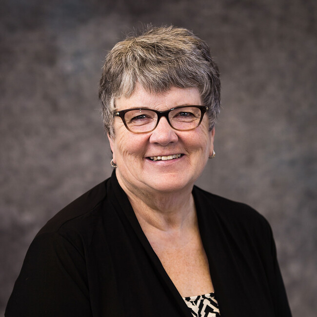 woman with short grey hair and glasses smiling for the camera