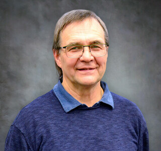 man wearing glasses and blue sweater smiling for the camera