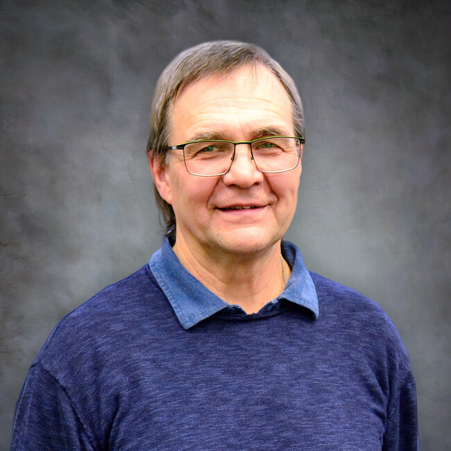 man wearing glasses and blue sweater smiling for the camera