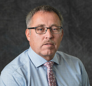 man wearing glasses and a shirt and tie smiling for the camera