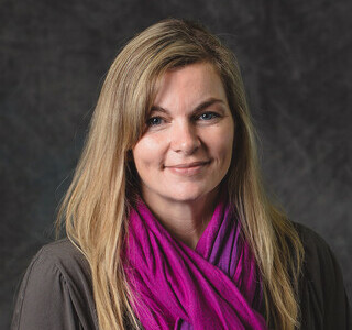 woman with long blonde hair wearing a brightly colored scarf smiling for the camera