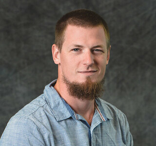 man in checked shirt with beard smiling for the camera