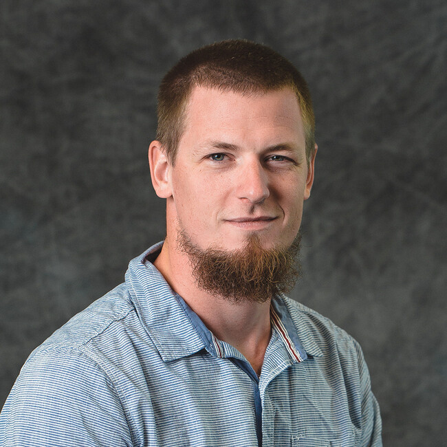 man in checked shirt with beard smiling for the camera