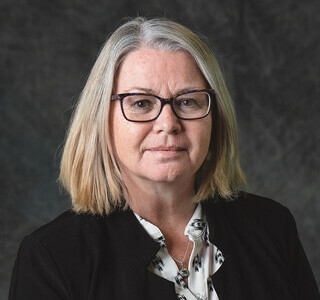 woman with grey shoulder length hair and glasses smiling for the camera