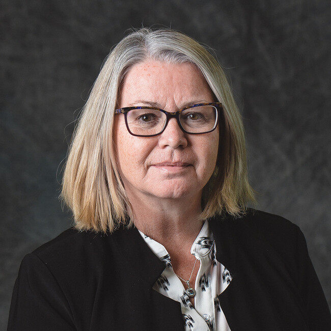 woman with grey shoulder length hair and glasses smiling for the camera