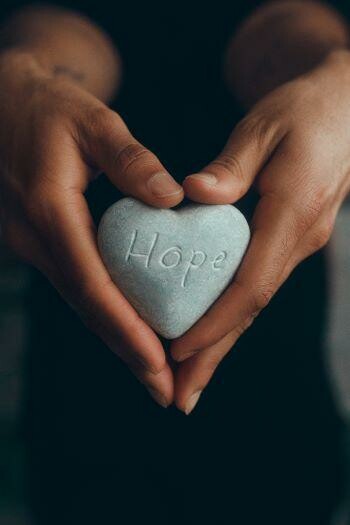 hands holding heart shaped rock that reads hope