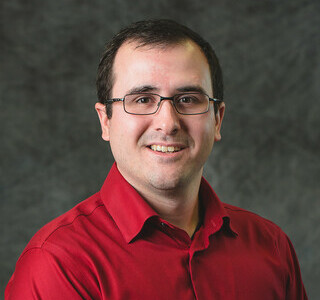 man in glasses and dark red shirt smiling for the camera