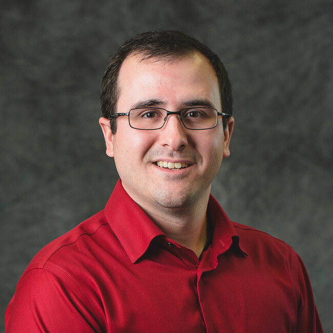 man in glasses and dark red shirt smiling for the camera